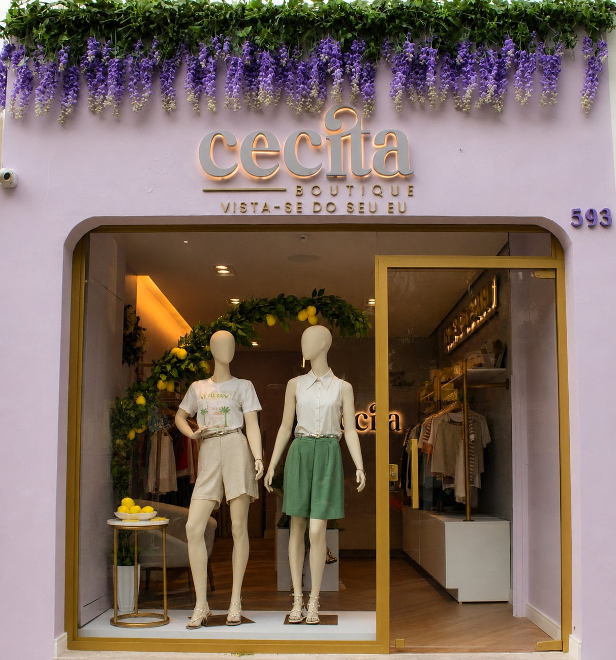 Fachada da boutique com vitrine, manequins e flores suspensas sobre a entrada