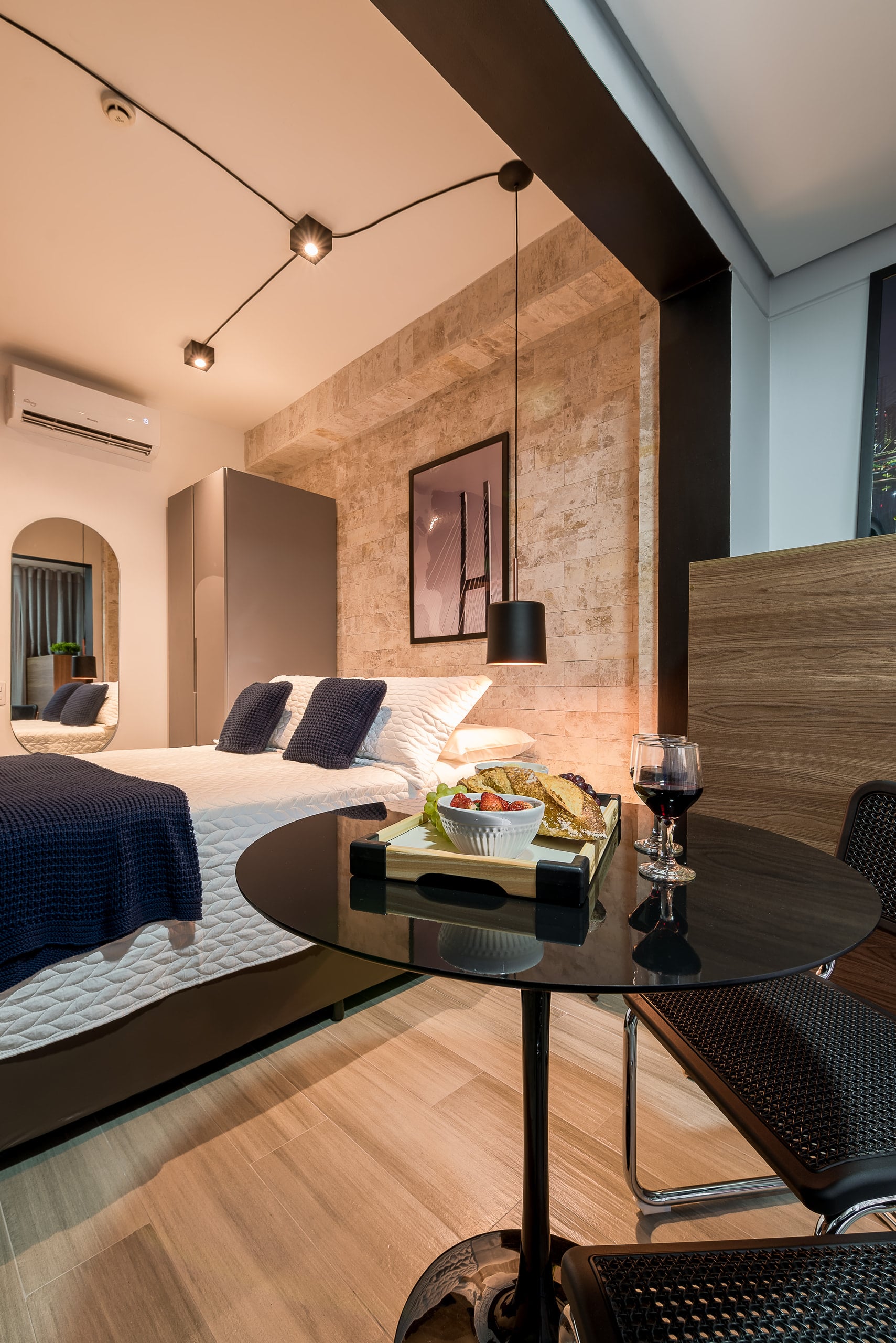 Mesa redonda posta em primeiro plano e a cama ao fundo, junto à janela