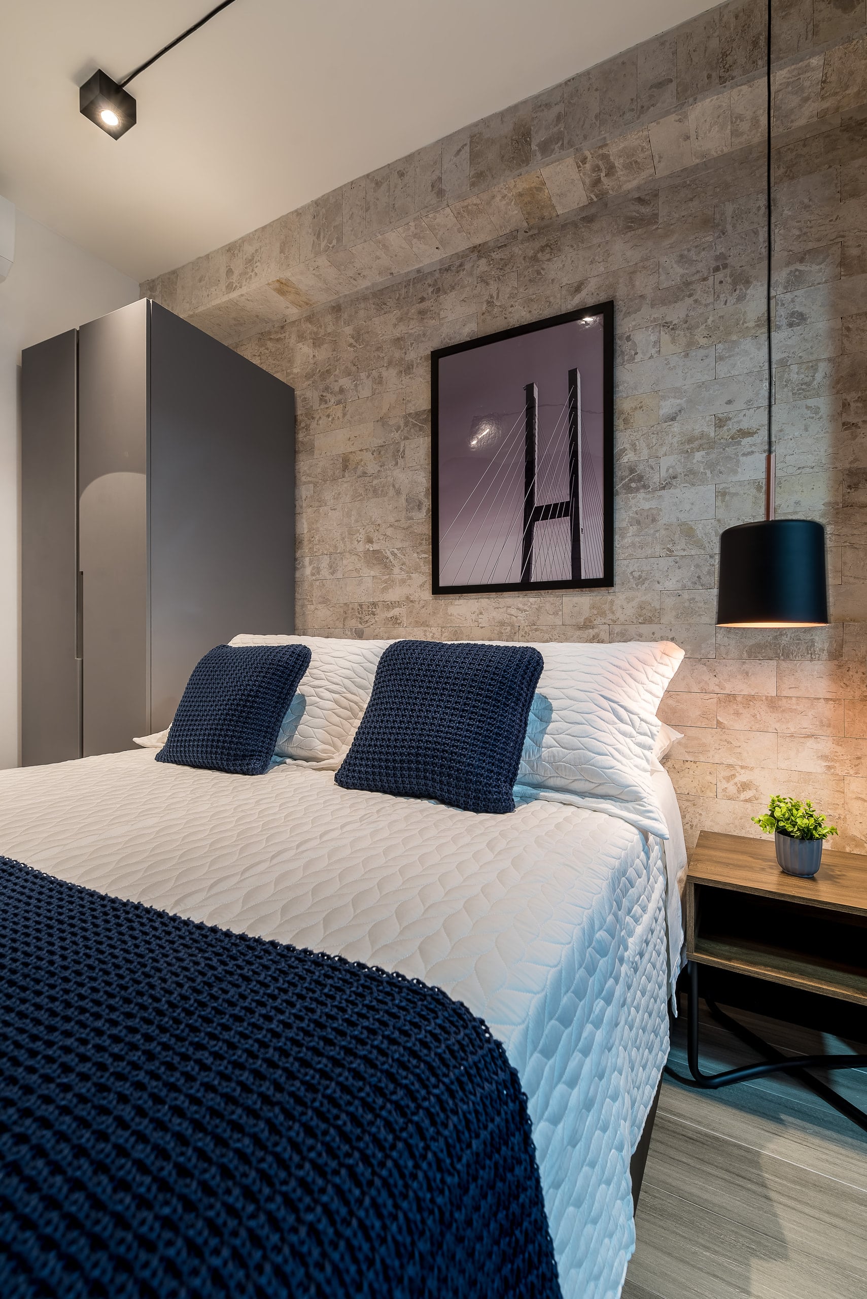 Cabeceira com revestimento de pedra, quadro e luminária pendente preta