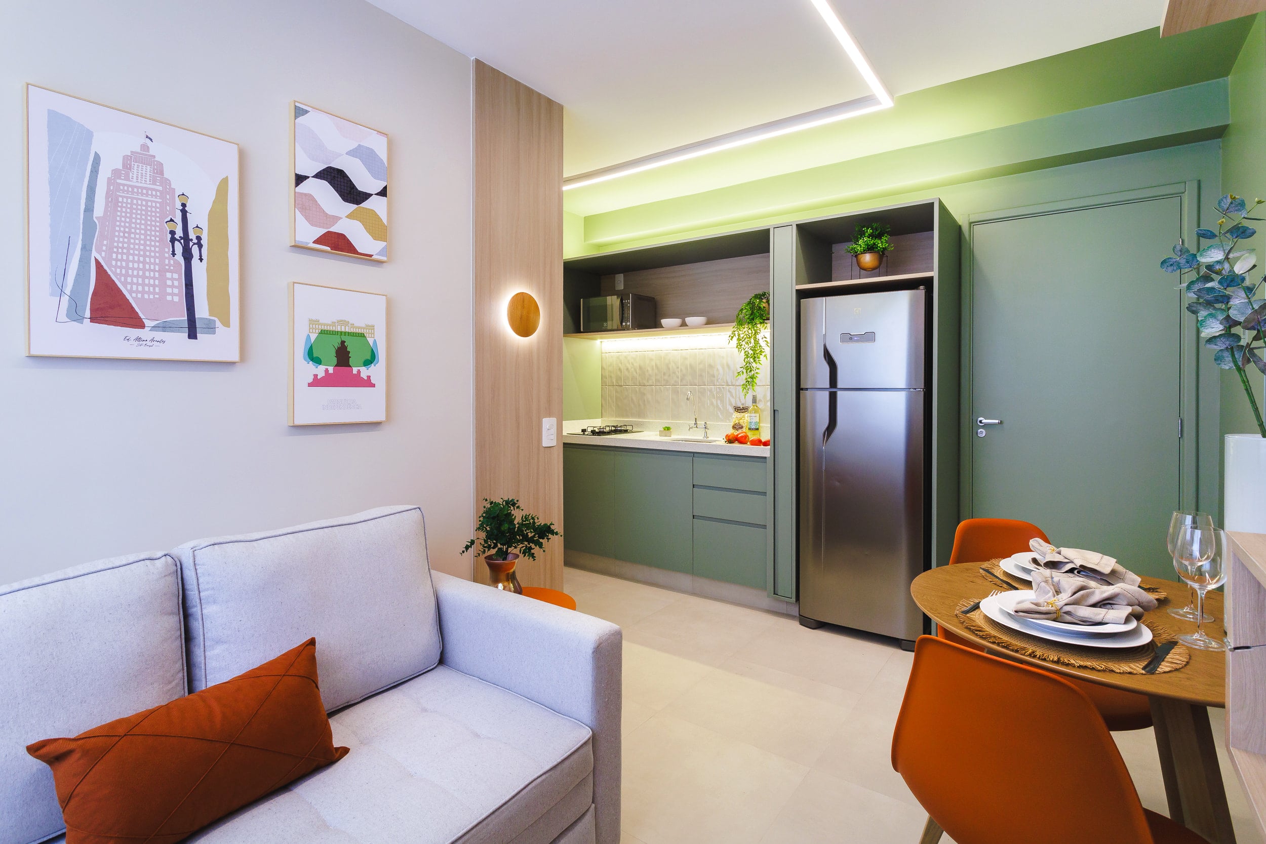 Studio integrado com sofá, mesa de jantar e cozinha verde ao fundo