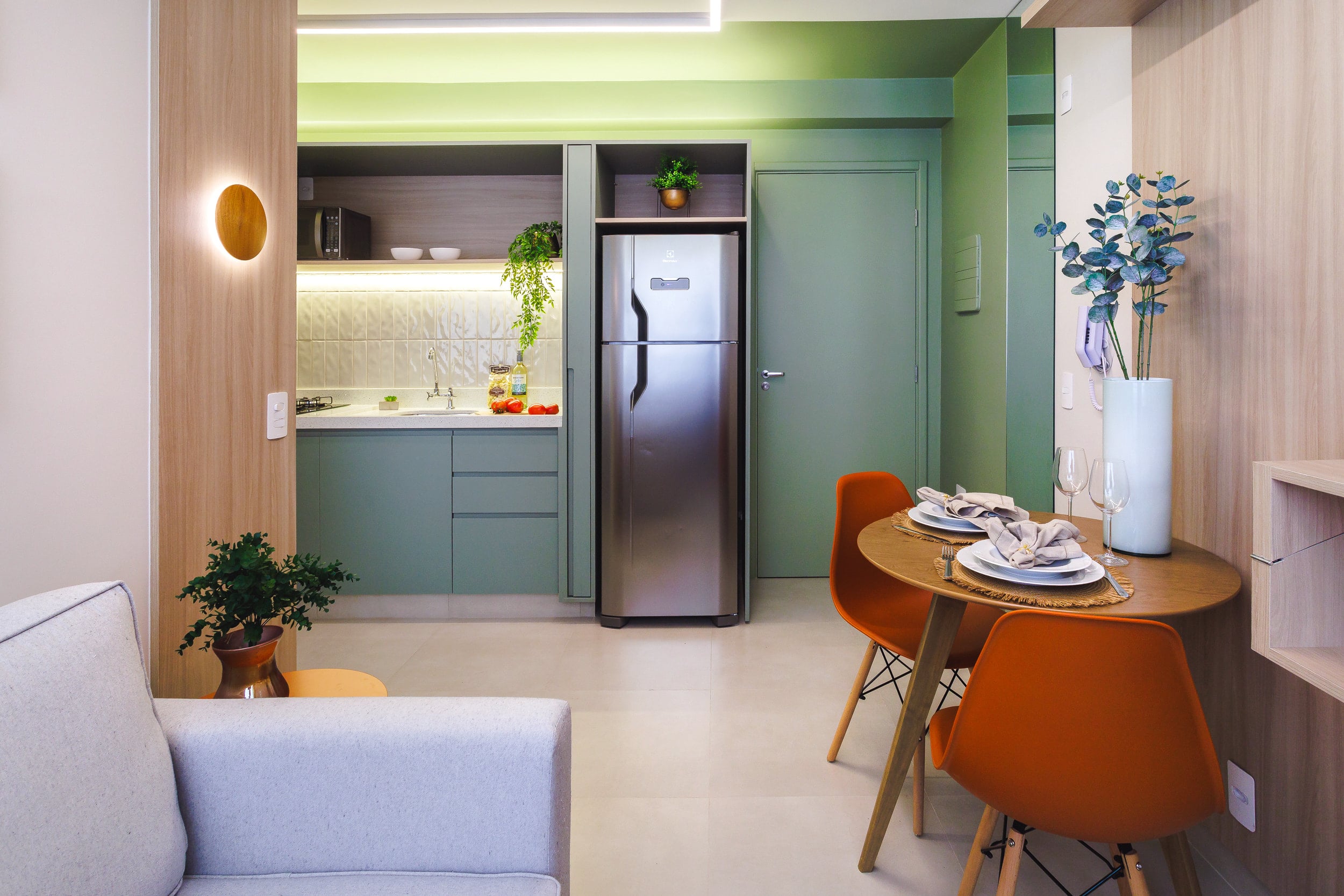 Cozinha compacta em marcenaria verde com geladeira embutida e mesa de refeições