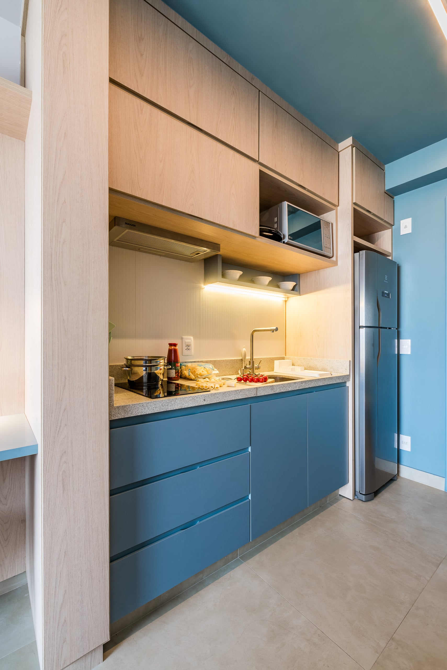 Bancada da cozinha vista de perto, com cooktop, cuba e armários suspensos