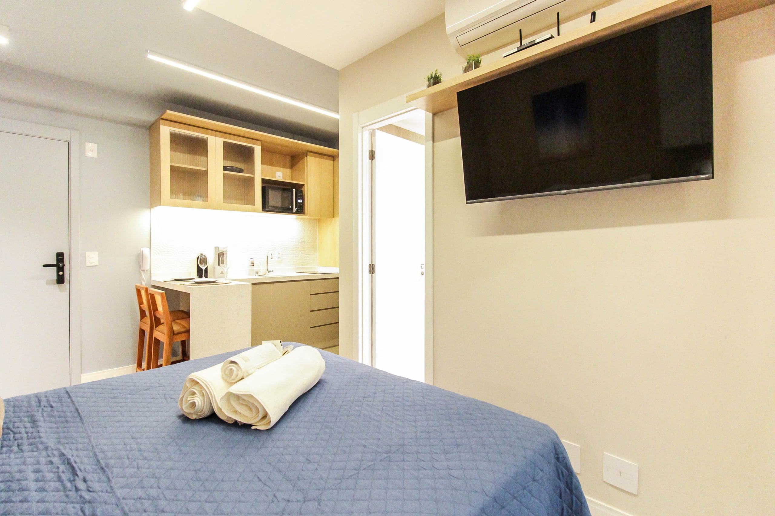 Studio com cama de casal, cozinha compacta e TV articulada na parede