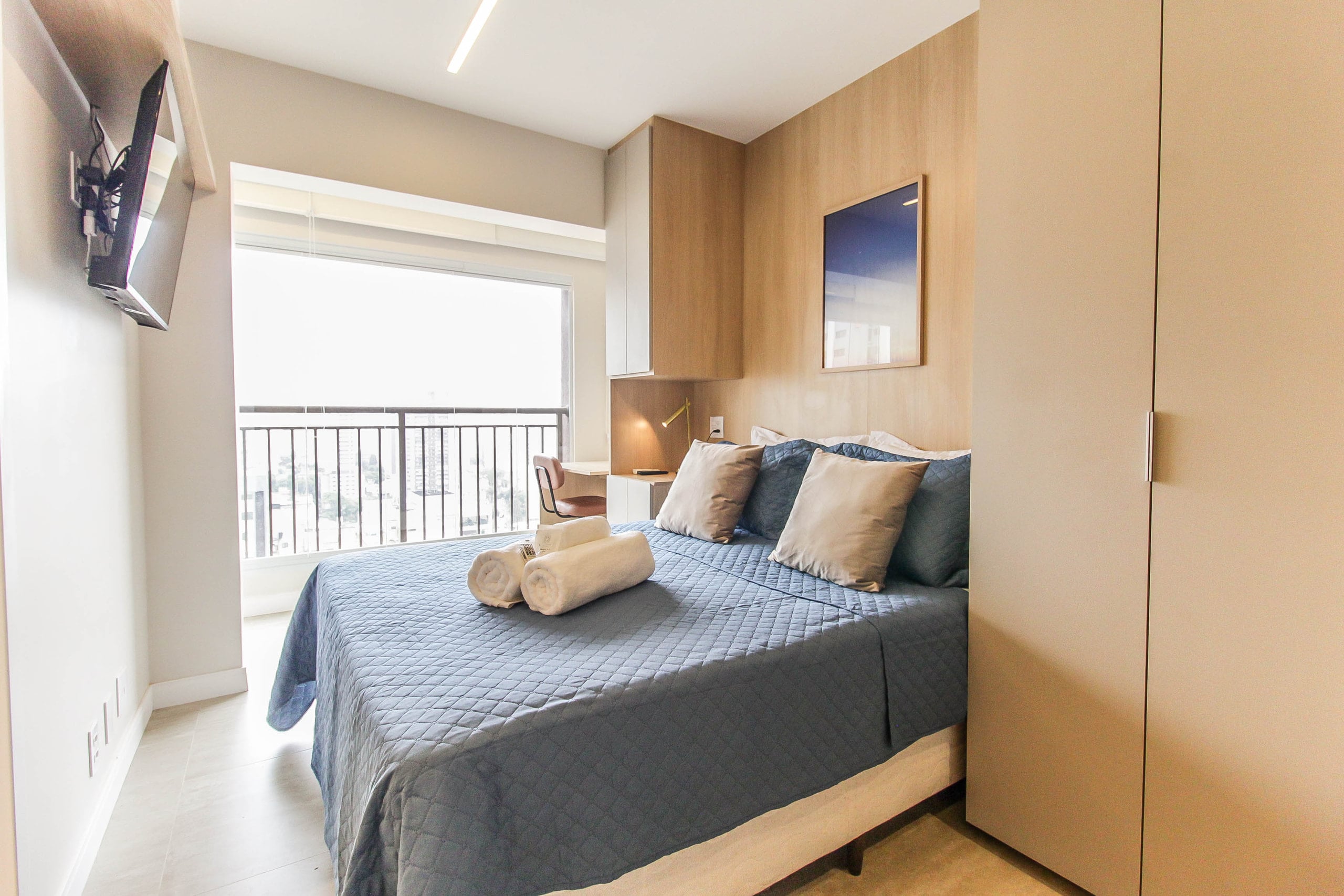 Cama junto à sacada, com luz natural entrando pela porta de vidro