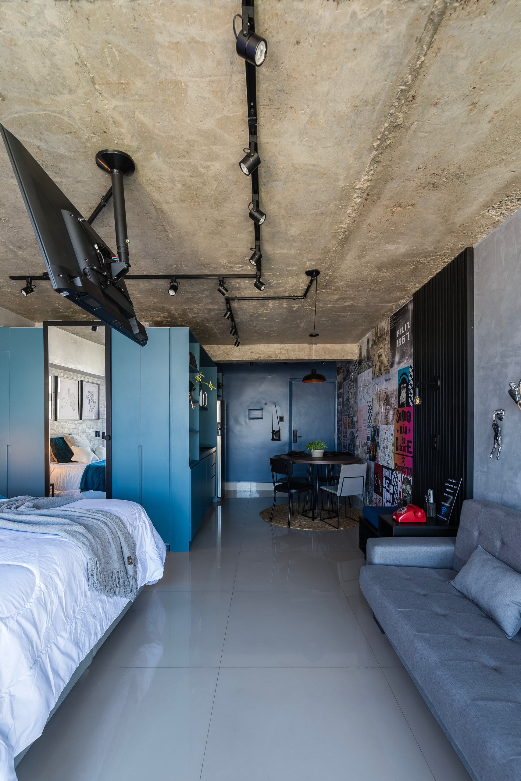 Loft com teto de concreto aparente, cama, cozinha azul e parede de grafite