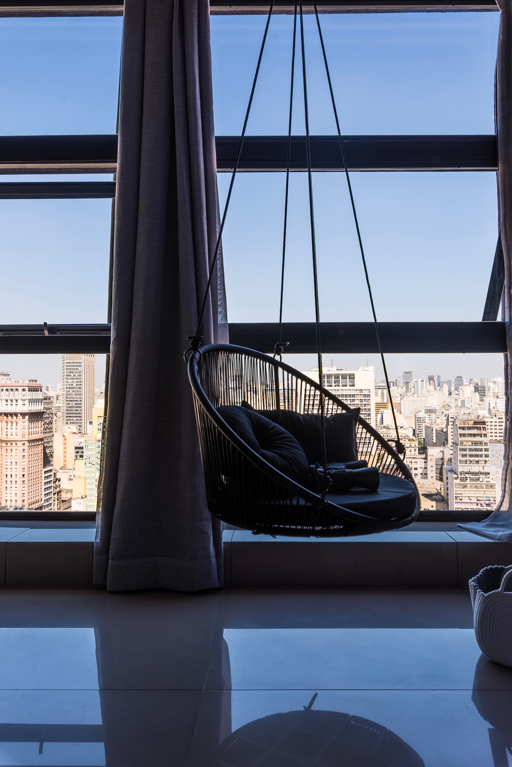 Poltrona suspensa junto à janela, com a vista do centro de São Paulo