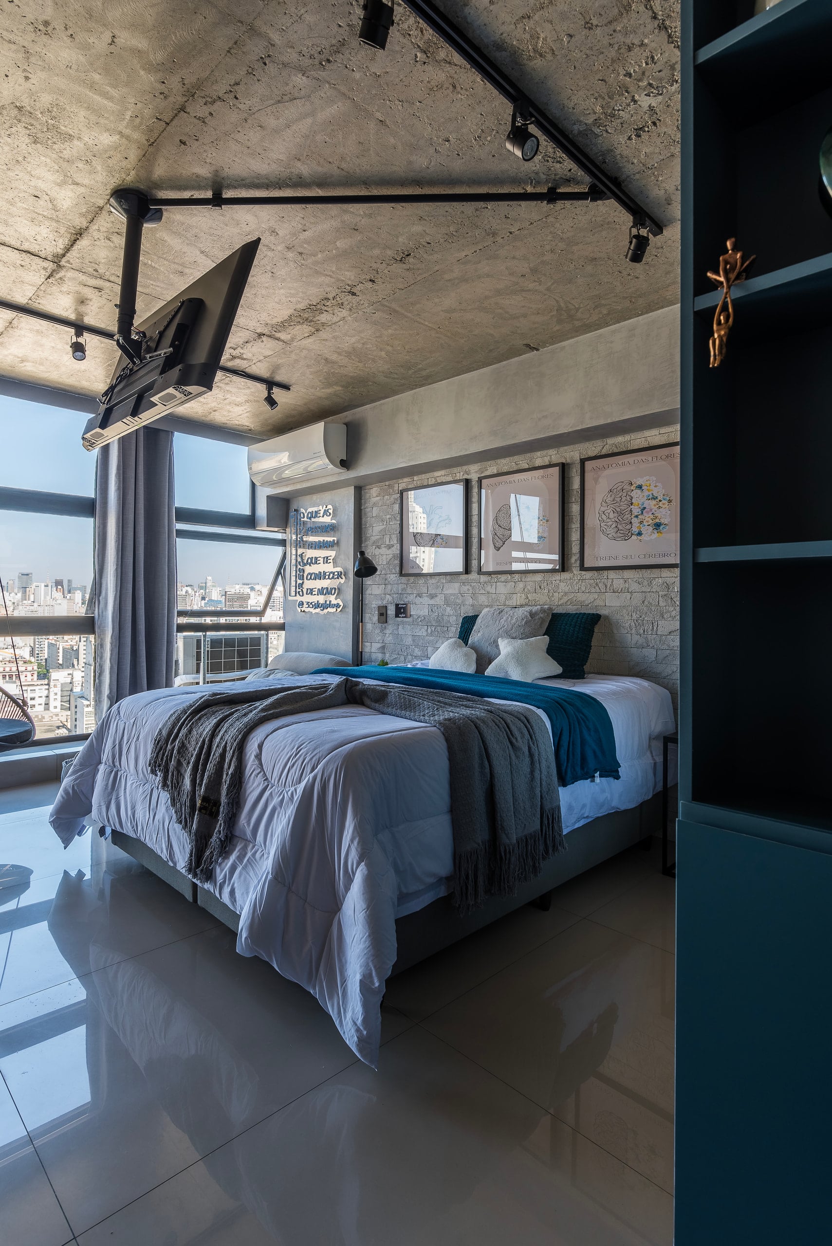 Cama de casal sob teto de concreto, com a cidade emoldurada pela janela