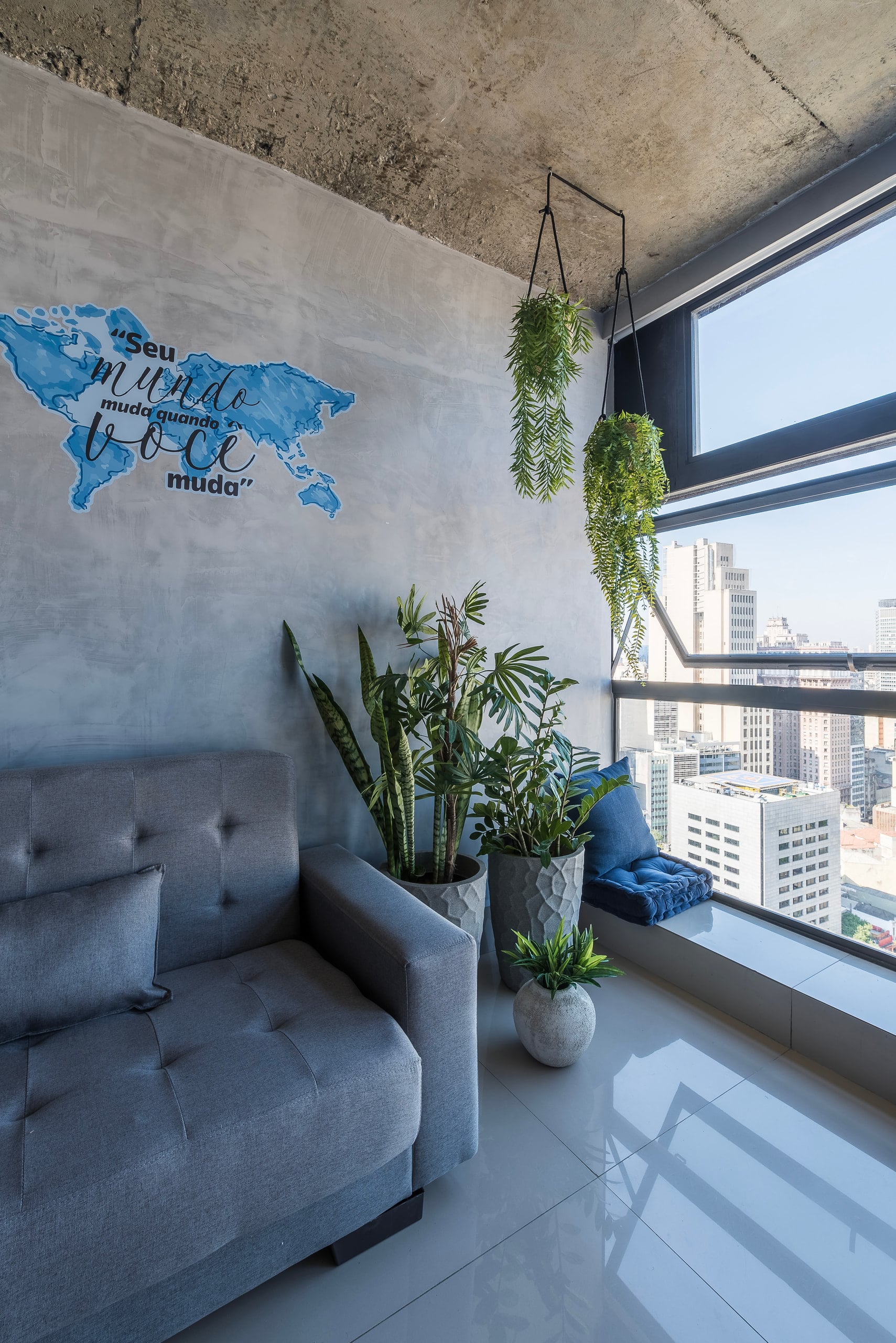 Estar com plantas e sofá junto à janela de canto, com vista para a cidade