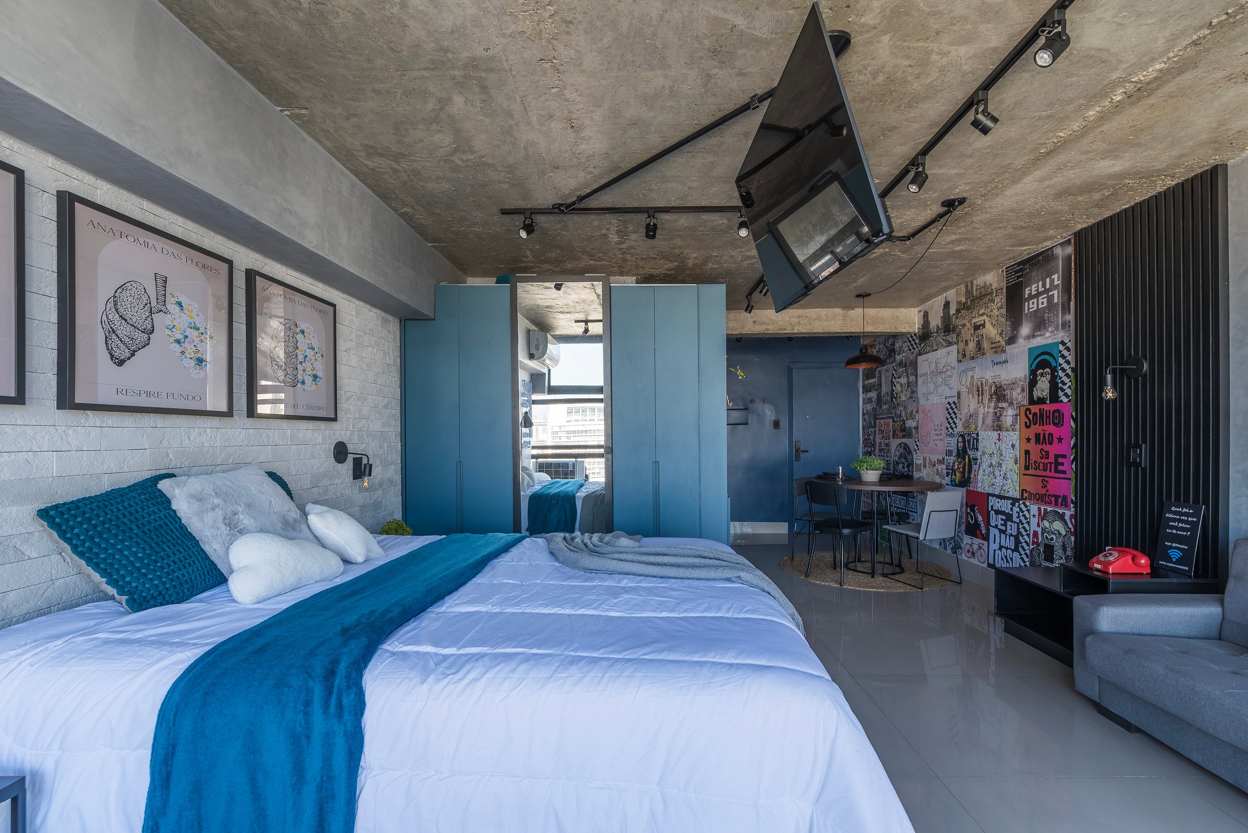 Cama vista de frente, com TV articulada e marcenaria azul ao fundo