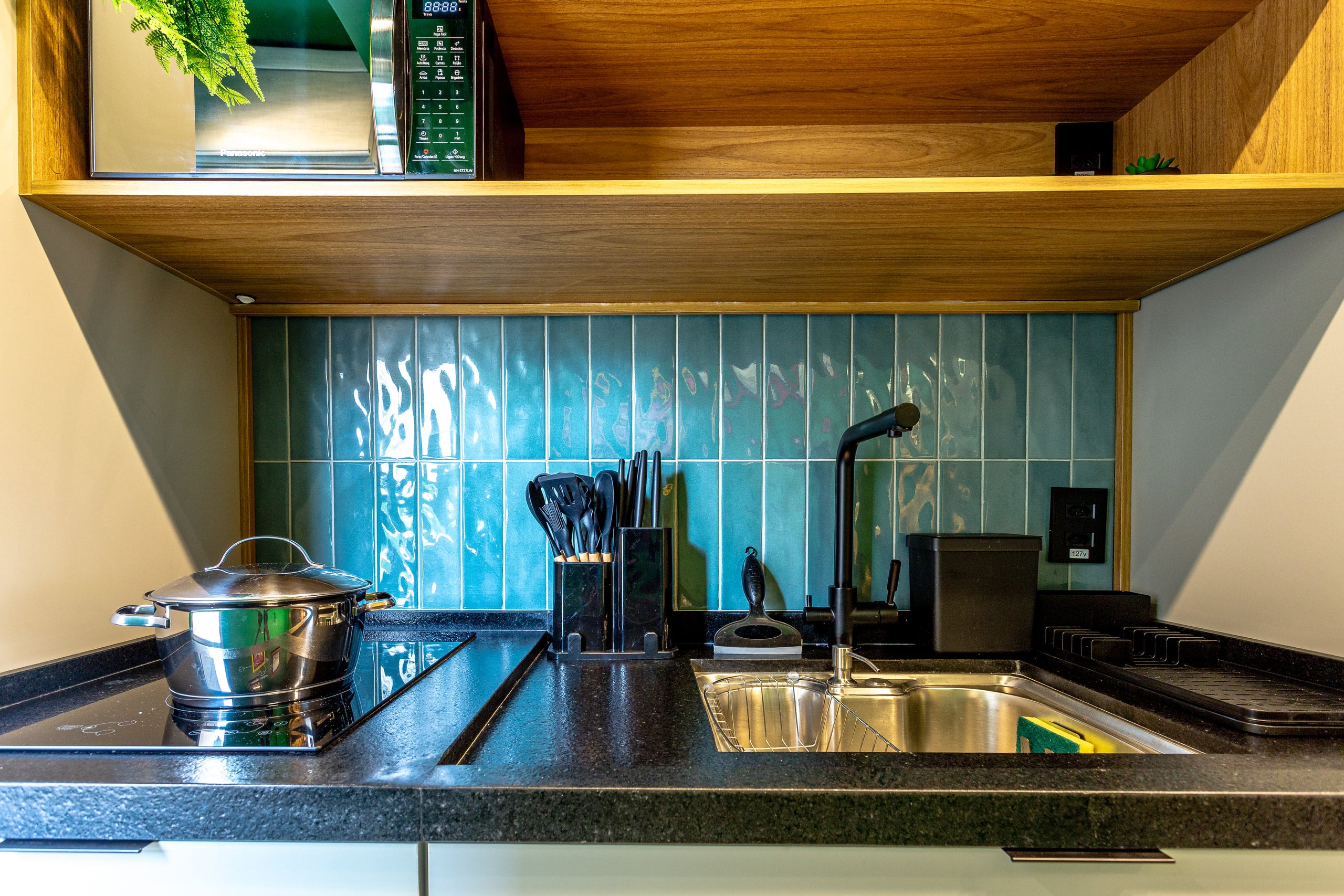 Detalhe do cooktop e da cuba sobre a bancada preta, com azulejo azul ao fundo