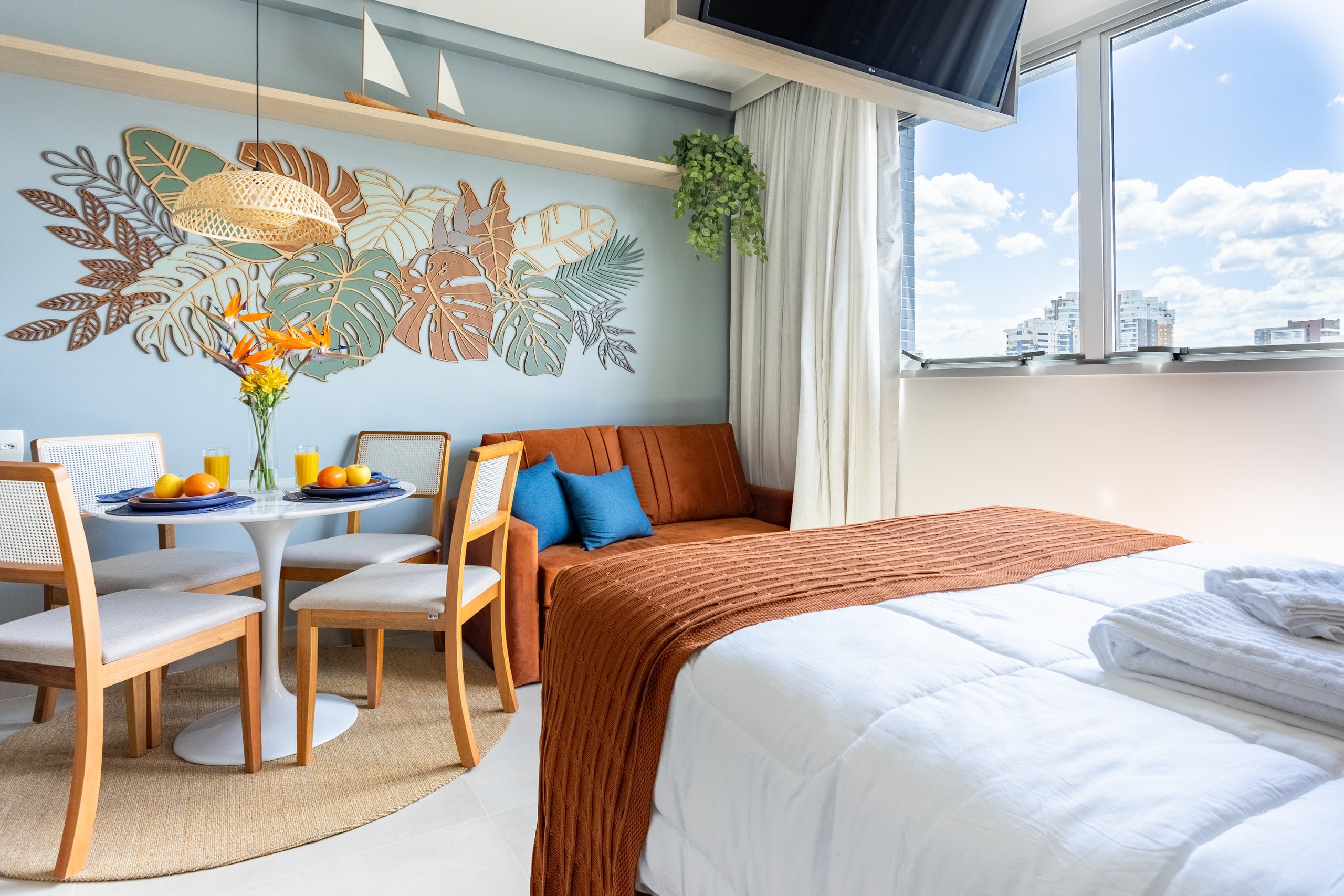 Studio com cama, mesa de refeições e parede azul com mural botânico
