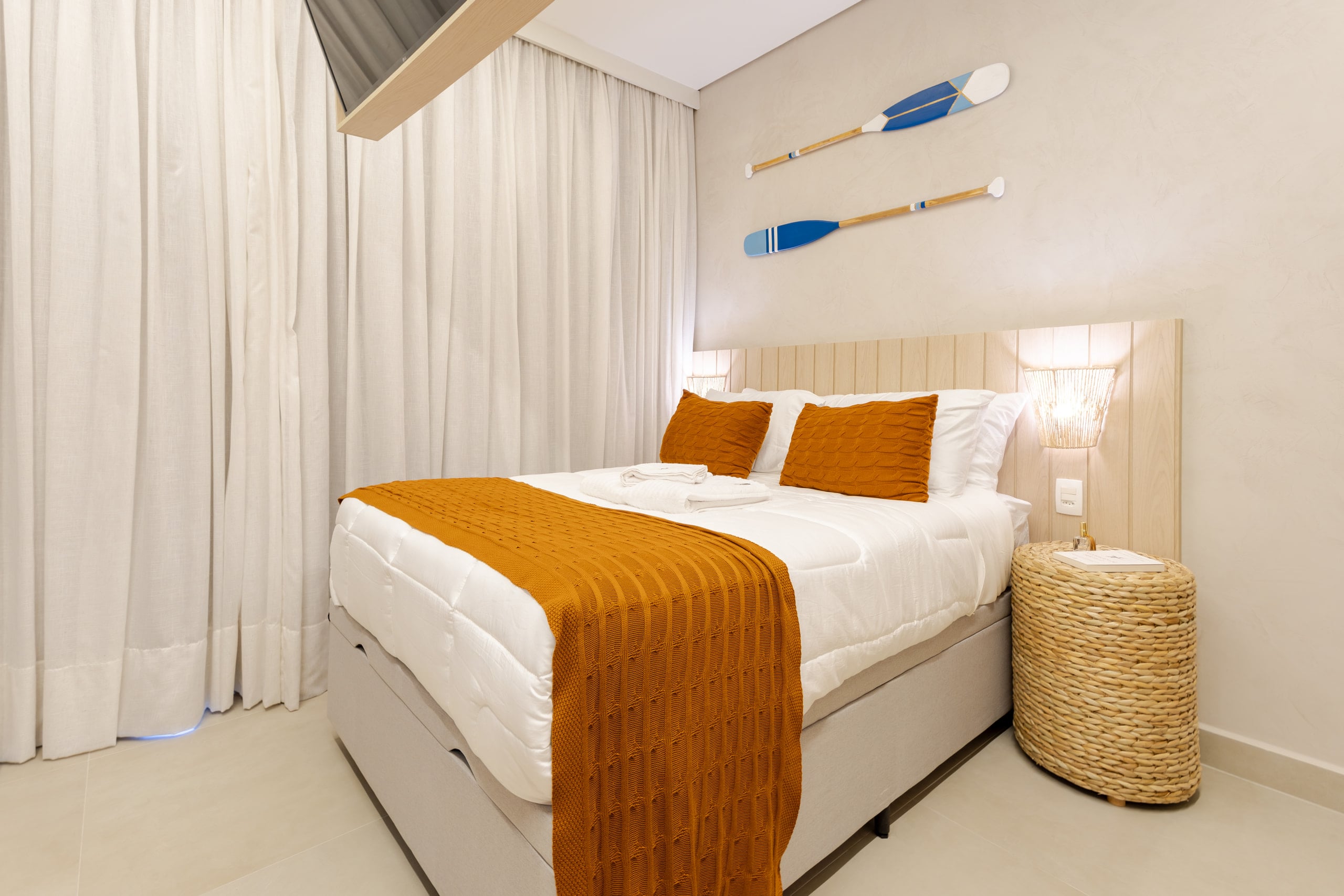 Cama de casal com manta laranja, remos decorativos na parede