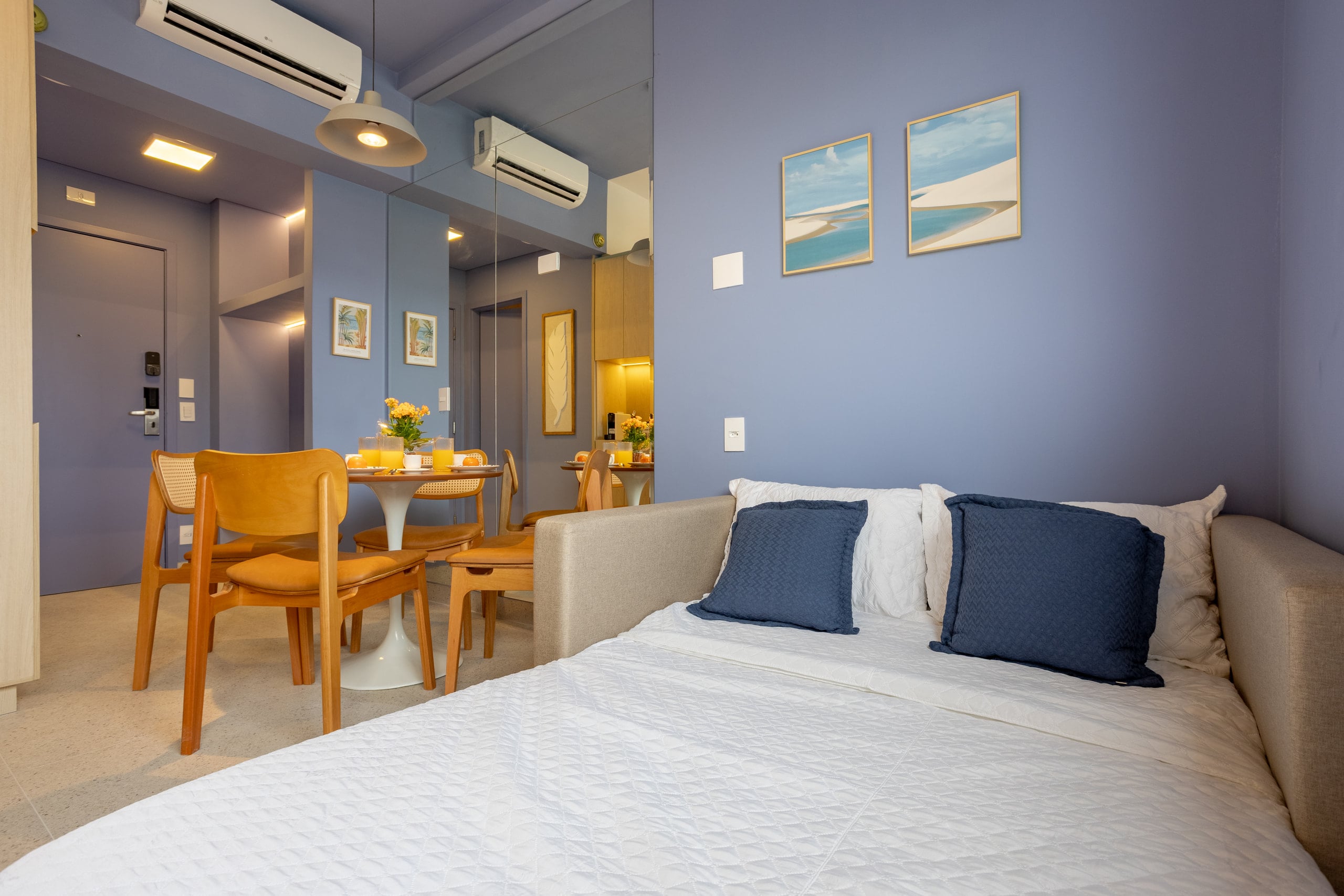Cama de casal com almofadas azuis e quadros de paisagem marinha