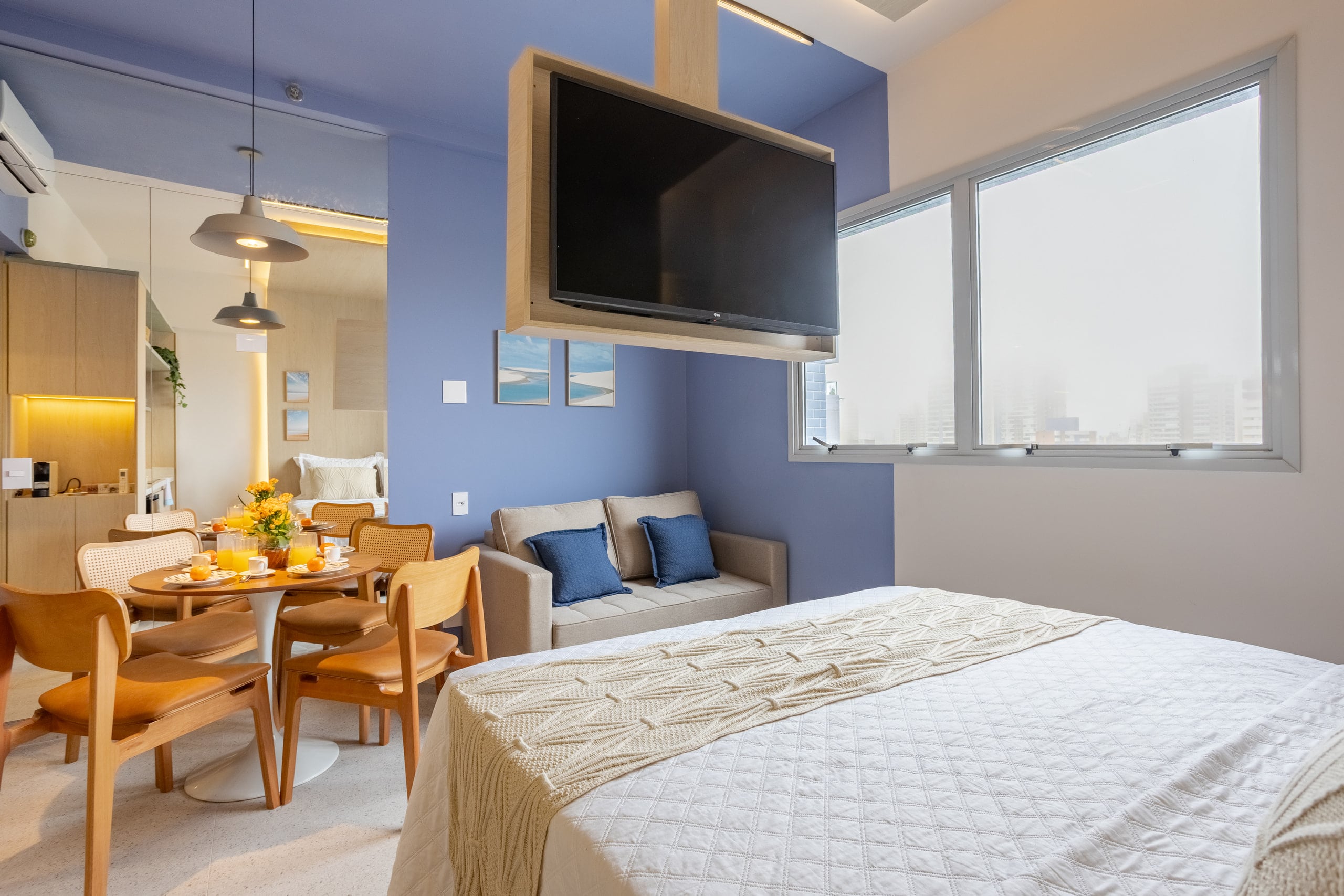 Cama vista de frente, com TV articulada e mesa de refeições ao lado