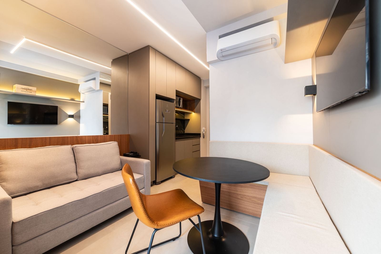 Sala de estar com sofá, poltrona caramelo e mesa redonda, cozinha ao fundo