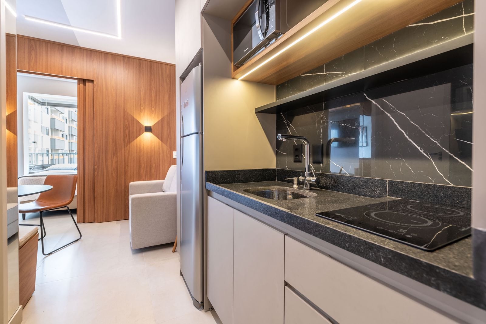 Cozinha compacta com bancada preta, cooktop e geladeira
