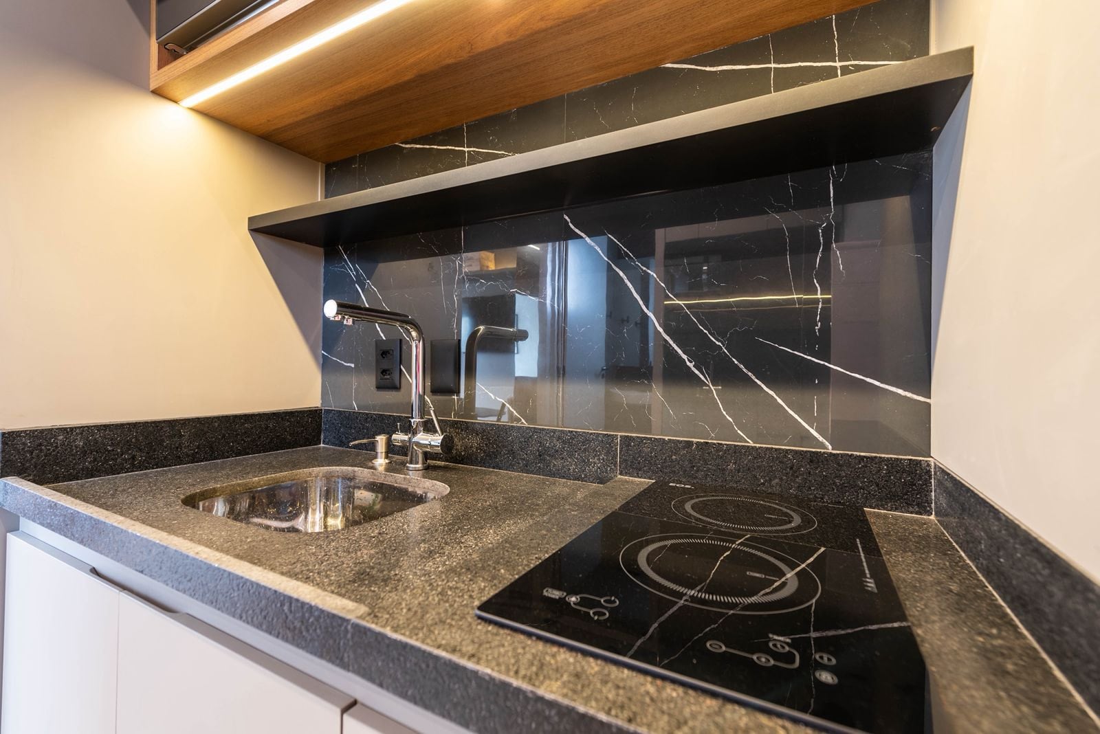 Detalhe da bancada da cozinha com cuba, cooktop e revestimento de mármore preto